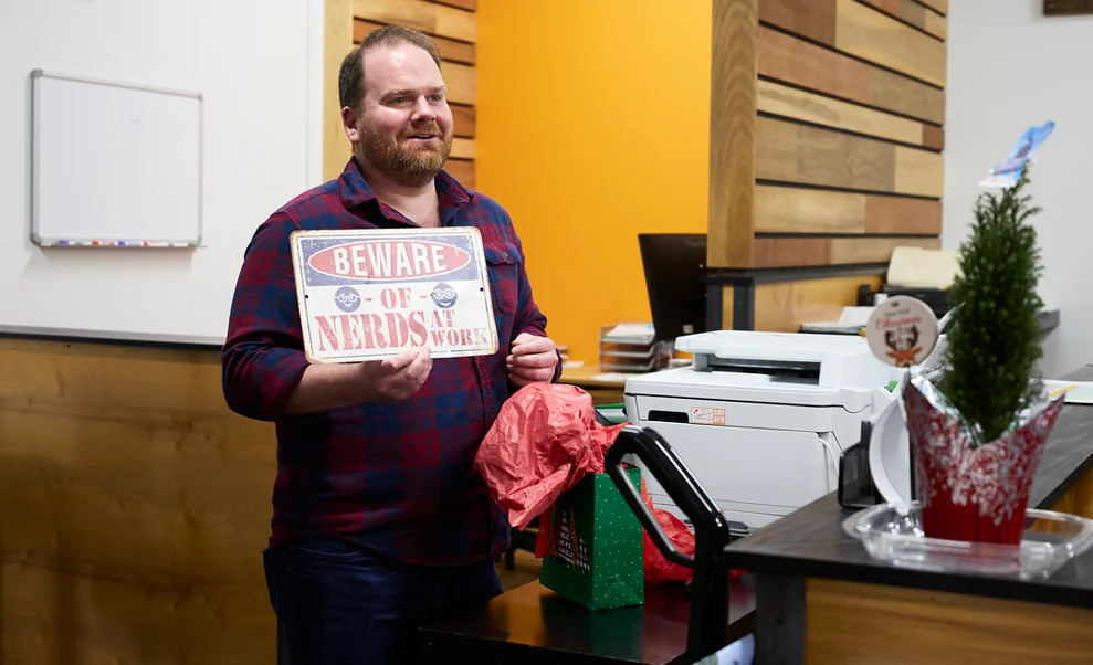 A Black Rock teammate holding a Beware of Nerds at Work sign during an office celebration